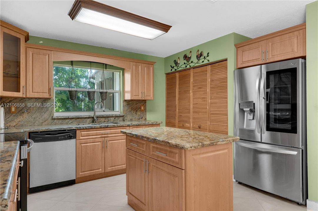 Kitchen featuring natural wood cabinetry, stone-surface countertops, stainless steel appliances, a central island, and louvered built-in pantry doors