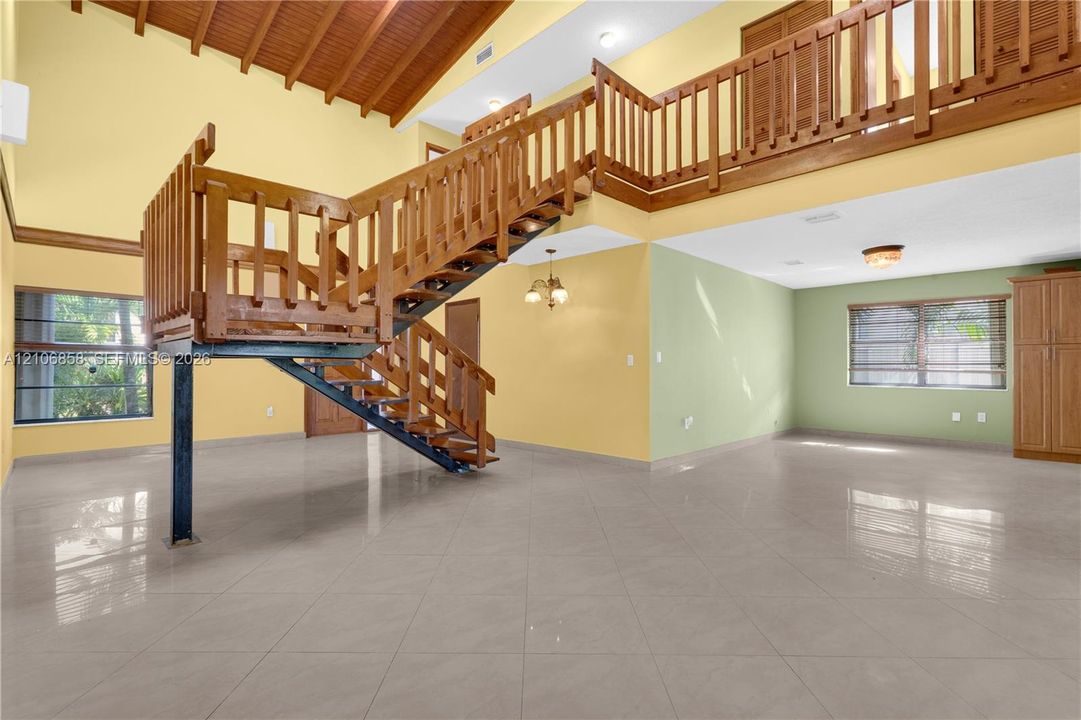 Vaulted wood-plank ceiling, structural metal staircase with wood railing, mezzanine balcony, large-format tile flooring, and built-in cabinetry