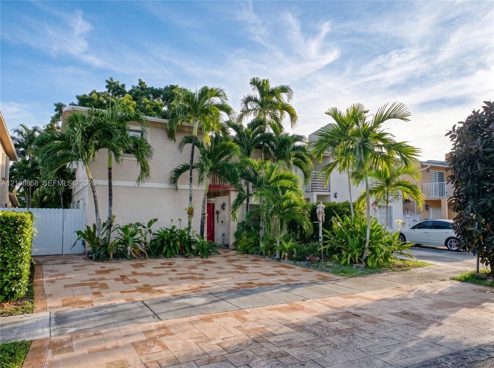 Multi-level exterior featuring a smooth stucco finish, paved driveway, second-story balcony, and established palm trees