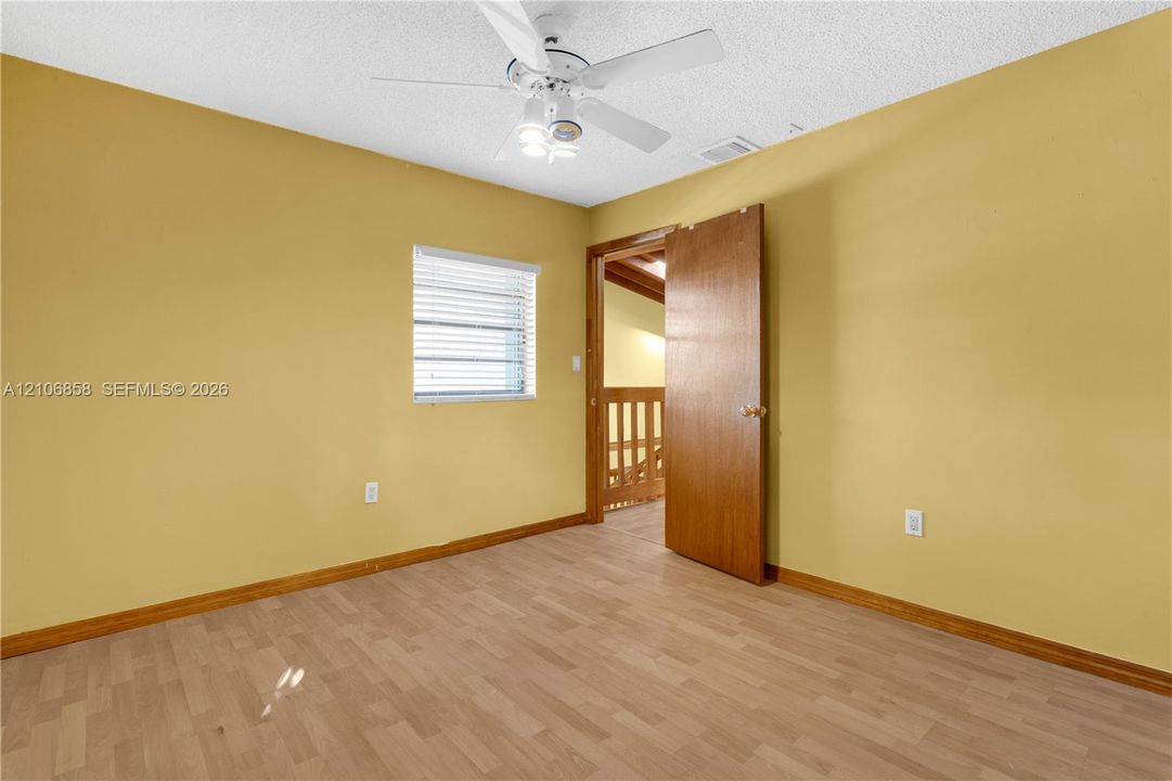Room featuring wood-finish flooring, a white ceiling fan with integrated lighting, and a window with horizontal blinds