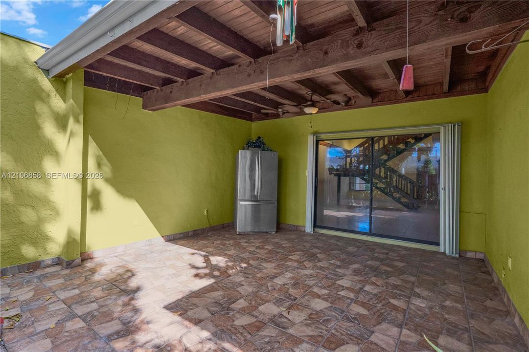 Covered patio featuring an exposed wood-beam ceiling, stone-tile flooring, ceiling fan, and sliding glass door