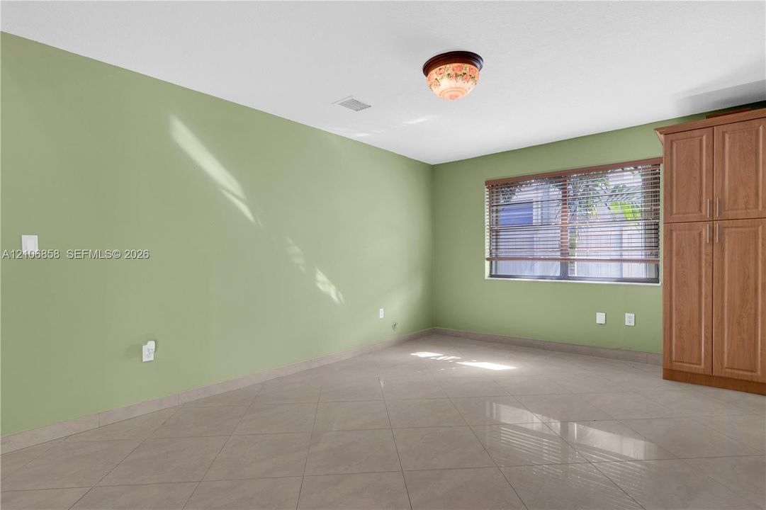 Room featuring large-format tile flooring, built-in wooden cabinetry, and a window with horizontal blinds