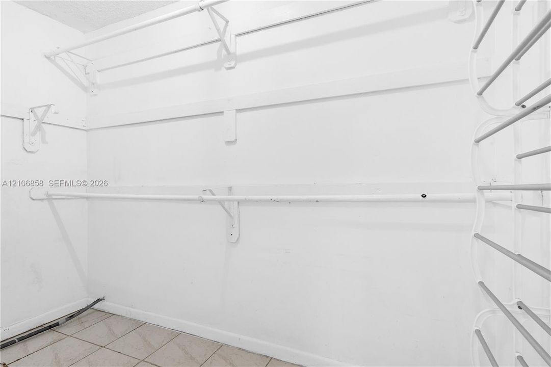 Storage area featuring white built-in shelving, metal garment rods, and ceramic tile flooring