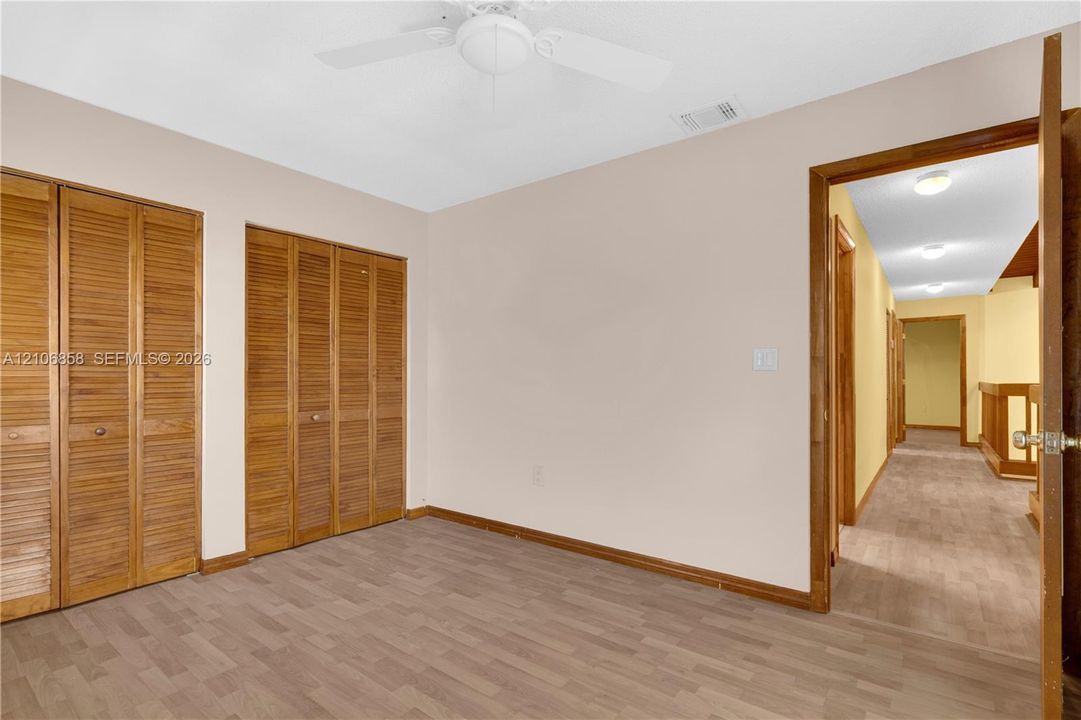 Room featuring wood-finish flooring, dual closets with louvered doors, and a ceiling fan