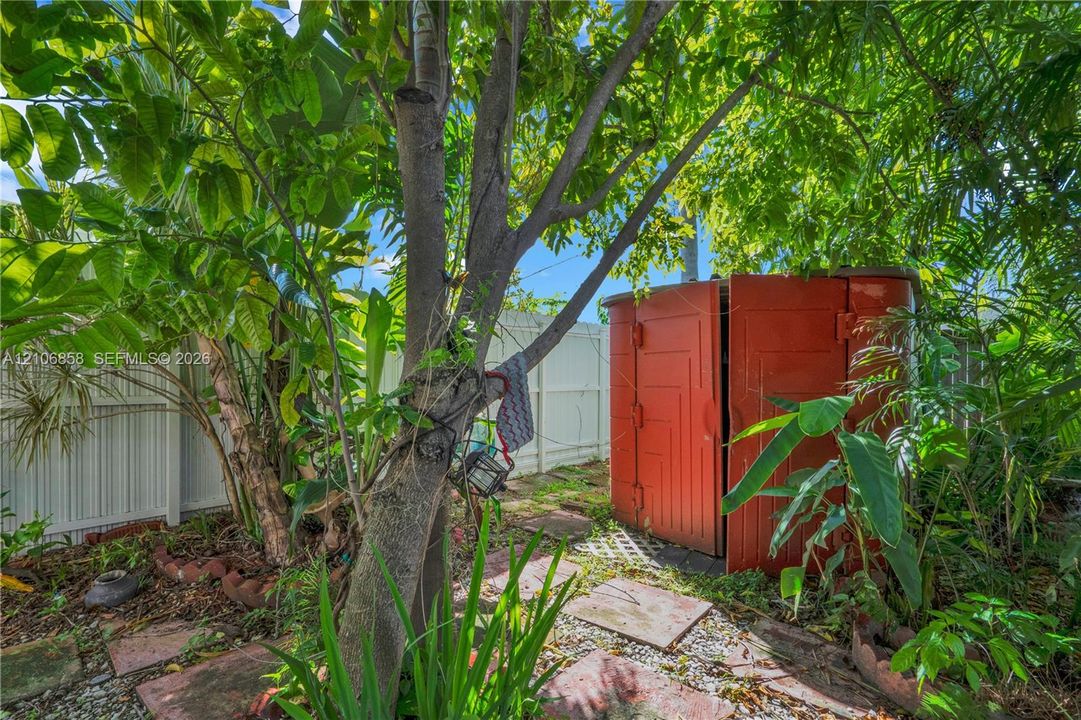 Private backyard featuring mature landscaping, a circular storage structure, stone paver pathway, and solid perimeter fencing