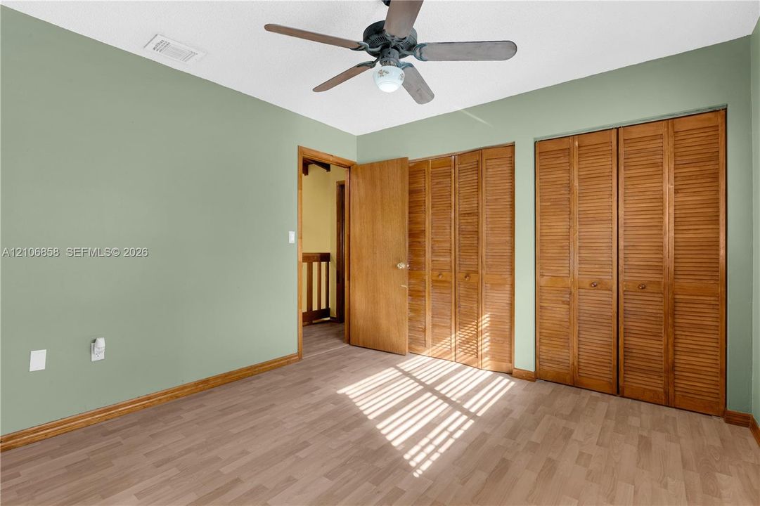 Room featuring wood-finish flooring, dual bi-fold louvered closet doors, and a ceiling fan