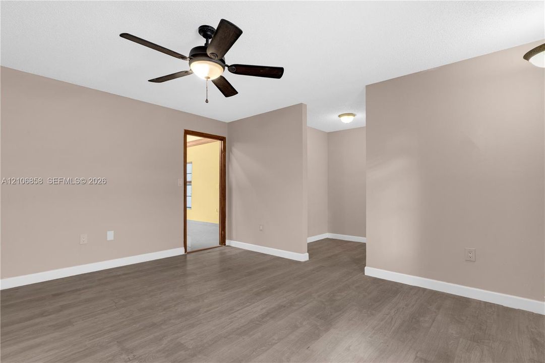 Interior space featuring neutral-toned walls, wood-finish flooring, a five-blade ceiling fan with integrated lighting, and multiple flush-mount ceiling light fixtures