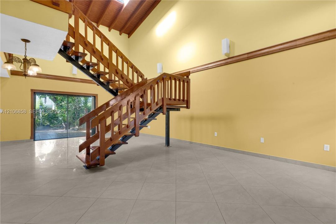 Vaulted ceiling with exposed wood-beam detailing, open-tread staircase with wood railings, large-format tile flooring, and oversized sliding glass doors