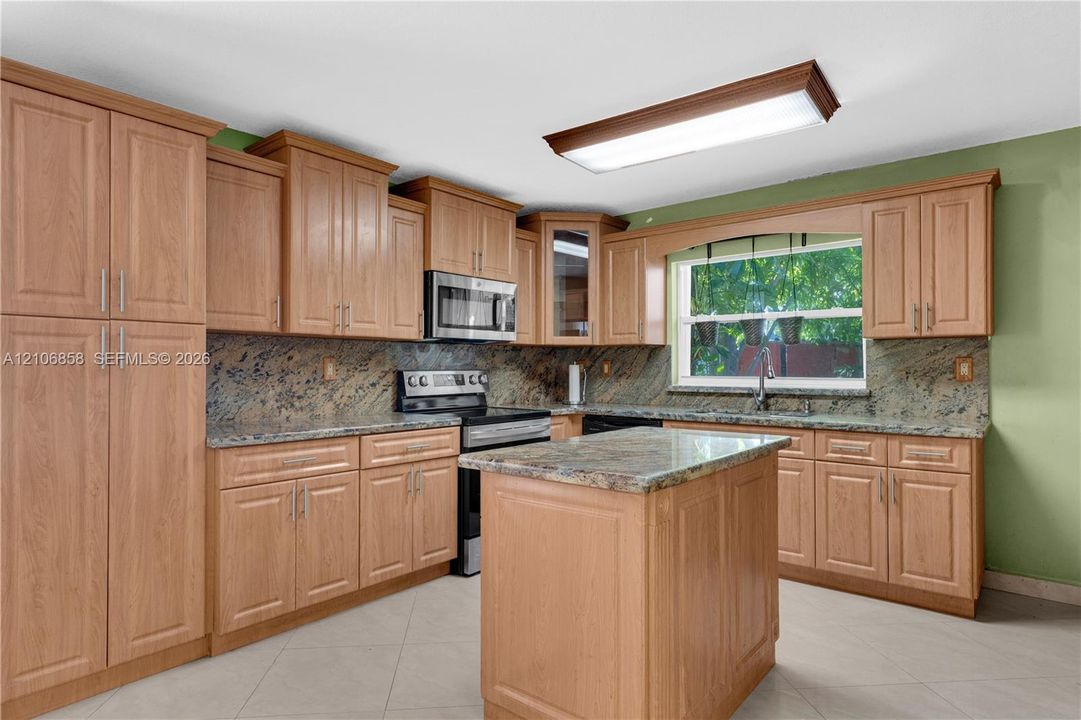 Kitchen featuring wood-finish cabinetry, natural stone countertops, a center island, stainless steel microwave, and tile flooring