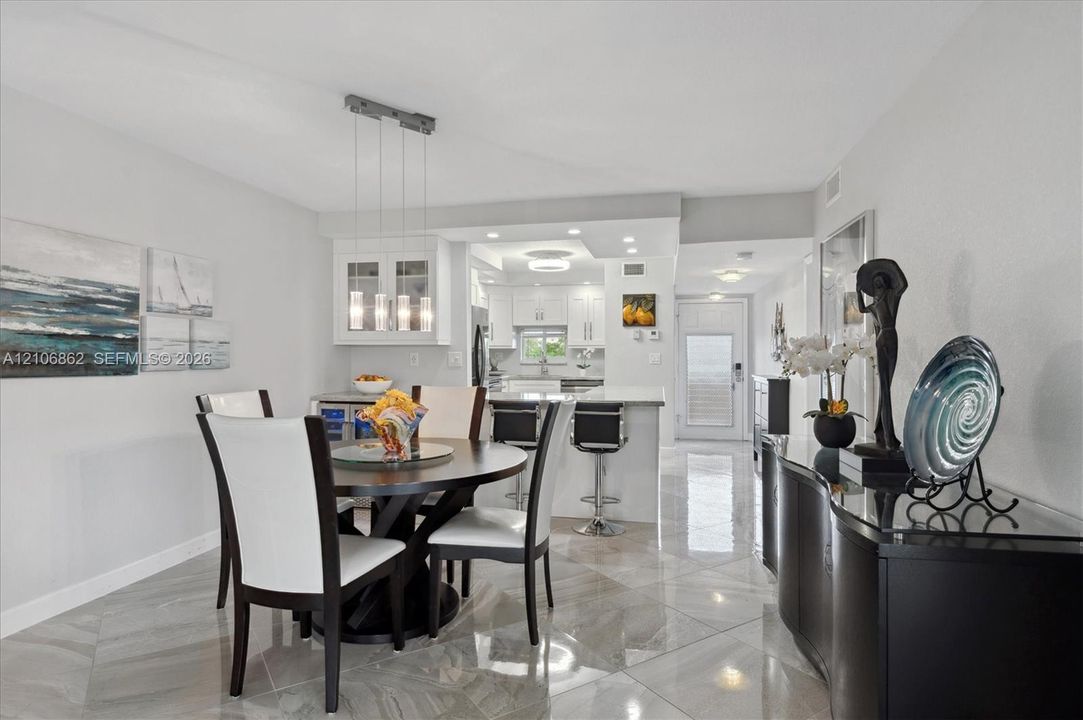 Open-concept interior featuring large-format tile flooring, a multi-pendant light fixture, glass-front upper cabinetry, and a peninsula with bar seating