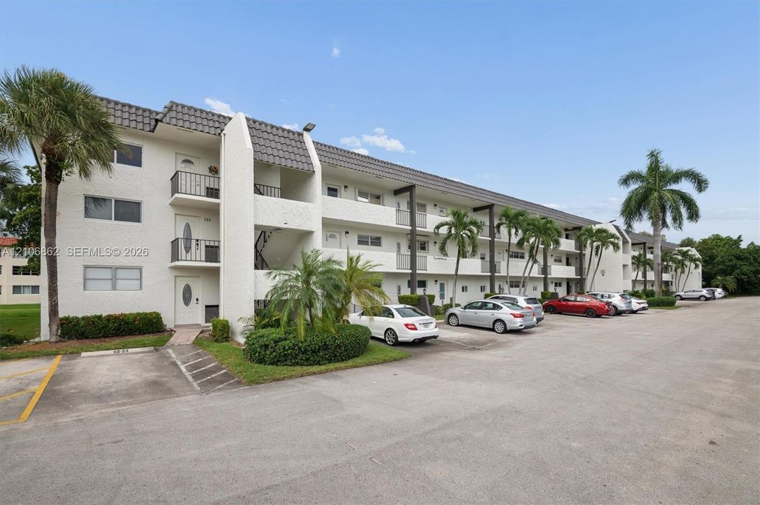 Multi-story stucco building exterior featuring a textured tile roof, private exterior balconies, and mature palm landscaping