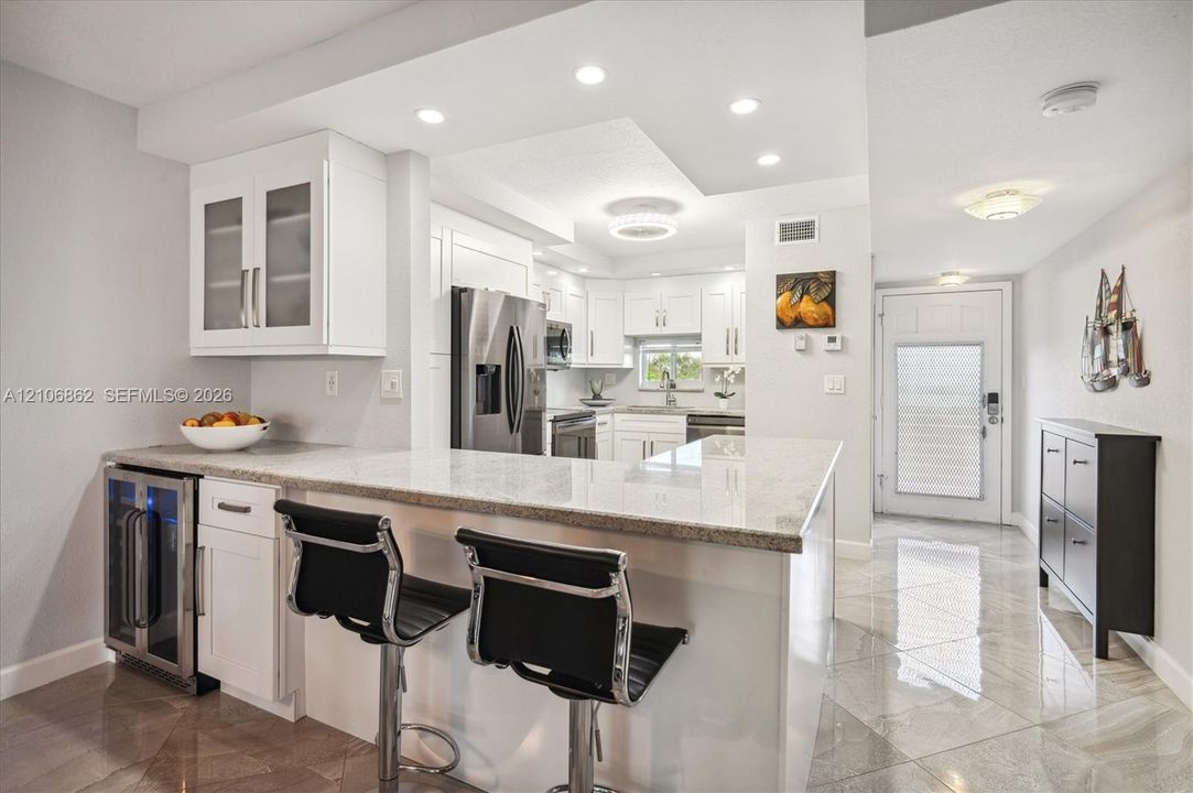 Kitchen featuring white cabinetry, light-toned stone countertops, built-in beverage refrigerator, stainless steel appliances, and large-format tile flooring