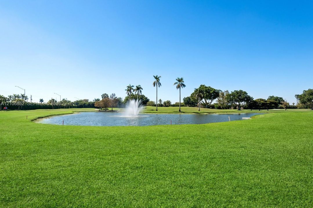 Expansive grounds featuring a manicured lawn, a central pond, a decorative water fountain, and mature palm trees