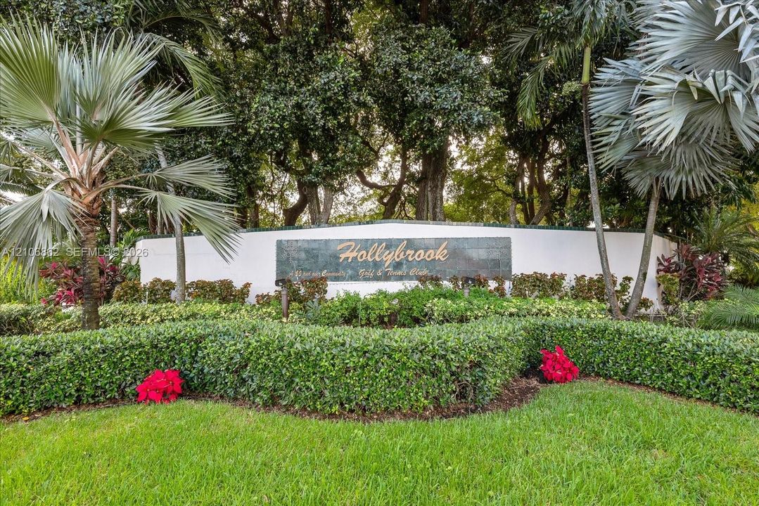 Hollybrook community entrance featuring manicured hedges, mature palm trees, and professional landscaping