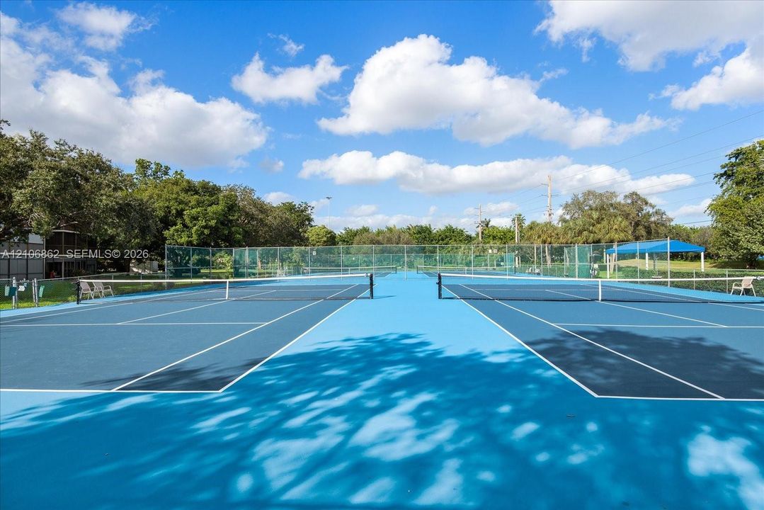 Dual tennis courts featuring a blue hard-court surface, perimeter fencing, and integrated net systems