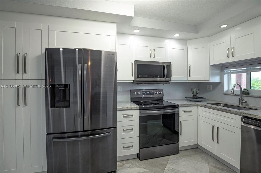 Kitchen featuring white shaker-style cabinetry, stainless steel appliances, speckled stone countertops, and recessed lighting