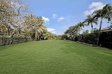 Aerial perspective featuring a residential property with a paved driveway, manicured lawn, mature palm trees, and an in-ground swimming pool