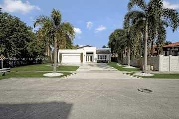 Single-story exterior featuring a concrete driveway, two-car garage, manicured lawn, and mature palm trees