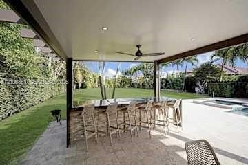 Rectangular swimming pool featuring a concrete deck and mature palm trees, bordered by a dense privacy hedge and synthetic turf area