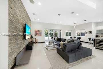 Open-concept living space featuring a floor-to-ceiling stone-veneer accent wall, large-format tile flooring, recessed lighting, and multi-panel sliding glass doors