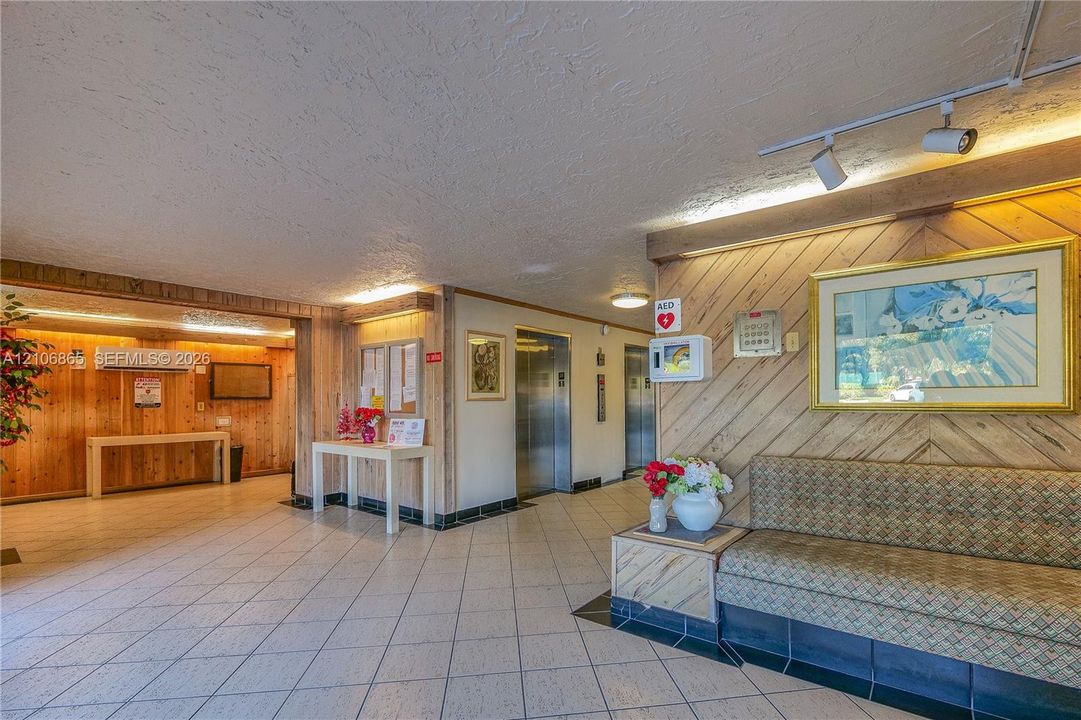 Lobby featuring diagonal wood-paneled accent walls, diamond-patterned tile flooring, track lighting, and dual elevators
