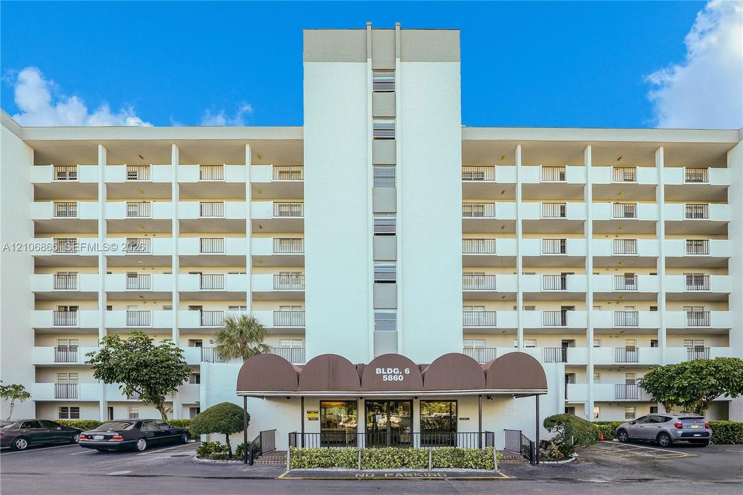 Multi-story exterior featuring a central arched entryway canopy, glass-front double-door entrance, and private balconies on each level