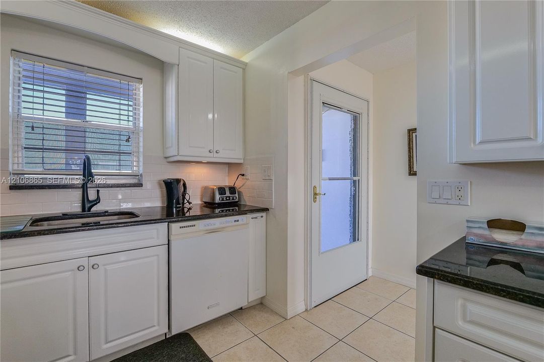 Kitchen featuring white cabinetry, dark stone countertops, tile backsplash, undermount sink with matte black faucet, and tiled flooring