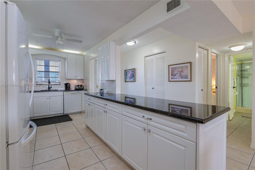 Kitchen featuring white cabinetry, dark stone-finish countertops, tile flooring, and integrated white appliances