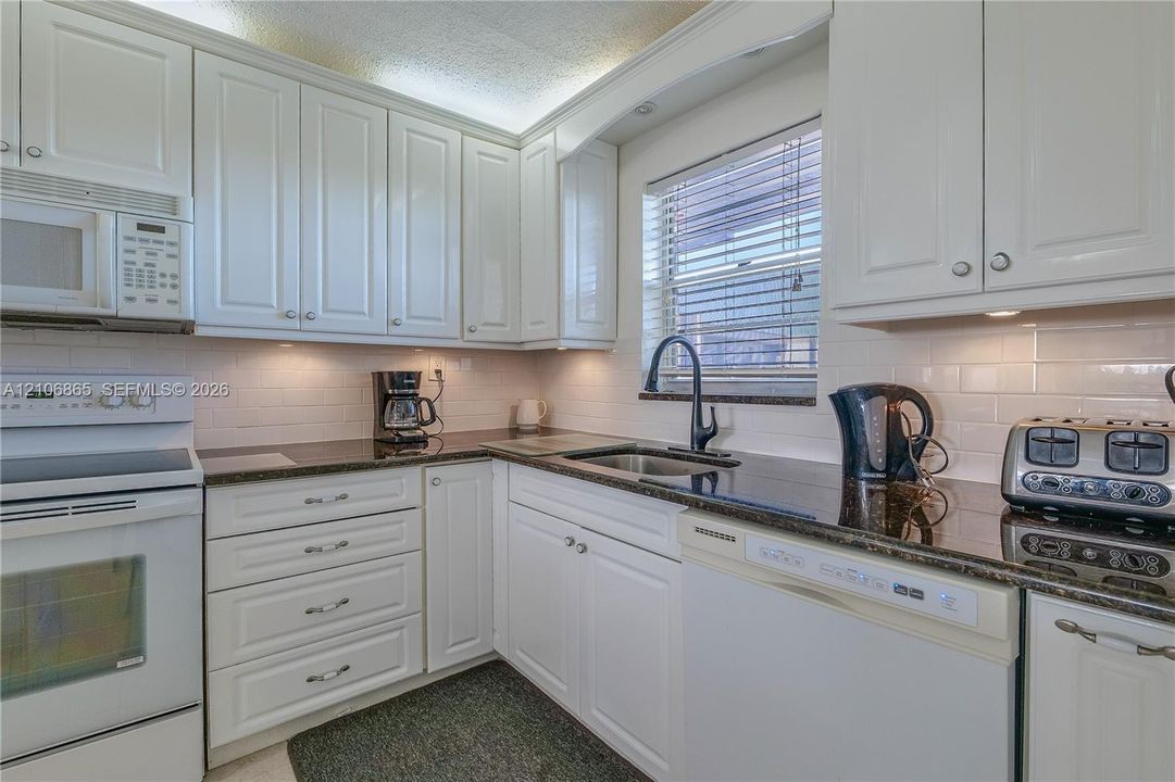 Kitchen featuring white cabinetry, dark stone countertops, white subway tile backsplash, undermount sink with a gooseneck faucet, and integrated appliances
