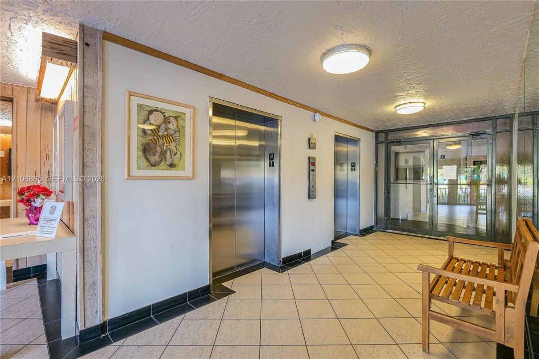 Common lobby area featuring dual elevators, ceramic tile flooring, and glass-paneled entry doors