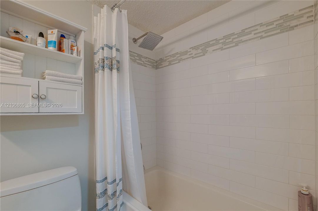 Bathroom featuring white subway tile wall surround with a linear glass accent inlay, square rainfall shower head, and white wall-mounted storage cabinetry