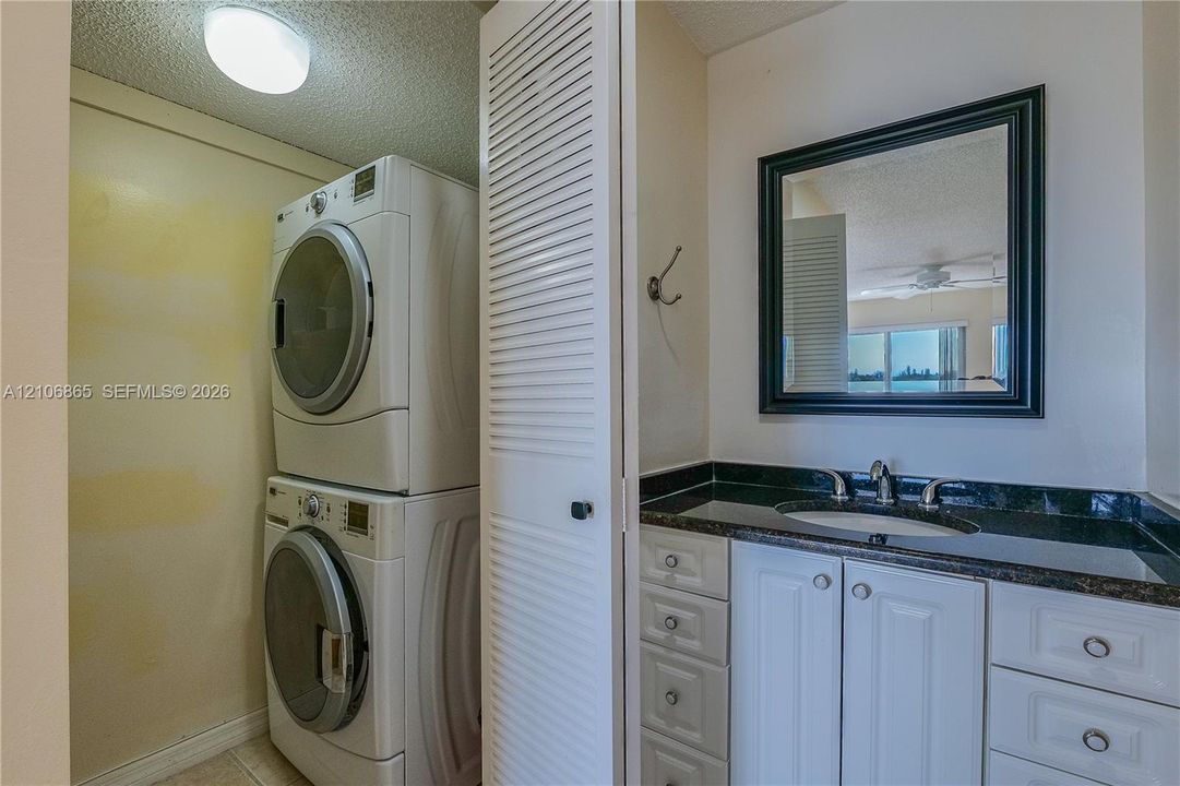 Laundry alcove featuring stacked laundry appliances and bi-fold louvered doors, accompanied by a vanity with a stone countertop, integrated sink, and framed wall mirror