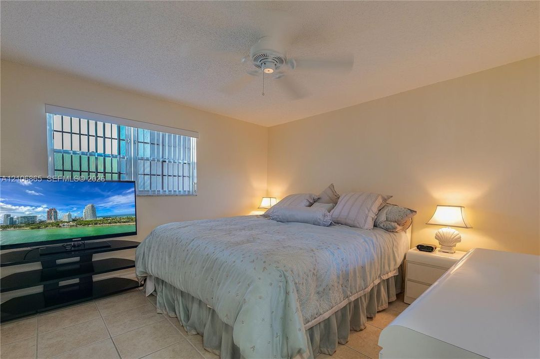Neutral-toned room featuring ceramic tile flooring, a central ceiling fan, and large window with integrated vertical blinds