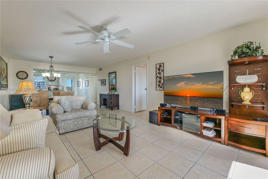 Living area featuring large format neutral floor tiling, recessed ceiling lighting, and a white ceiling fan