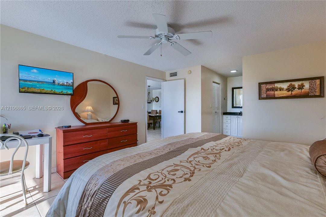 Neutral-toned walls paired with tile flooring, featuring a ceiling-mounted fan and a built-in vanity area with white cabinetry and dark countertops