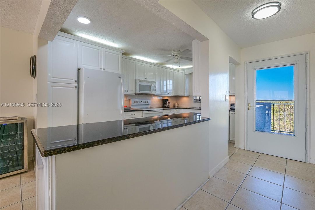 Kitchen featuring white cabinetry, dark stone-finish countertops, built-in white appliances, ceramic tile flooring, and exterior door access