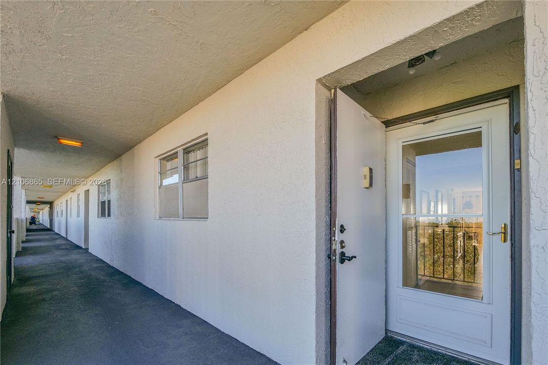 Exterior walkway featuring a textured stucco facade, metal-frame windows, and a white storm door with a central glass panel