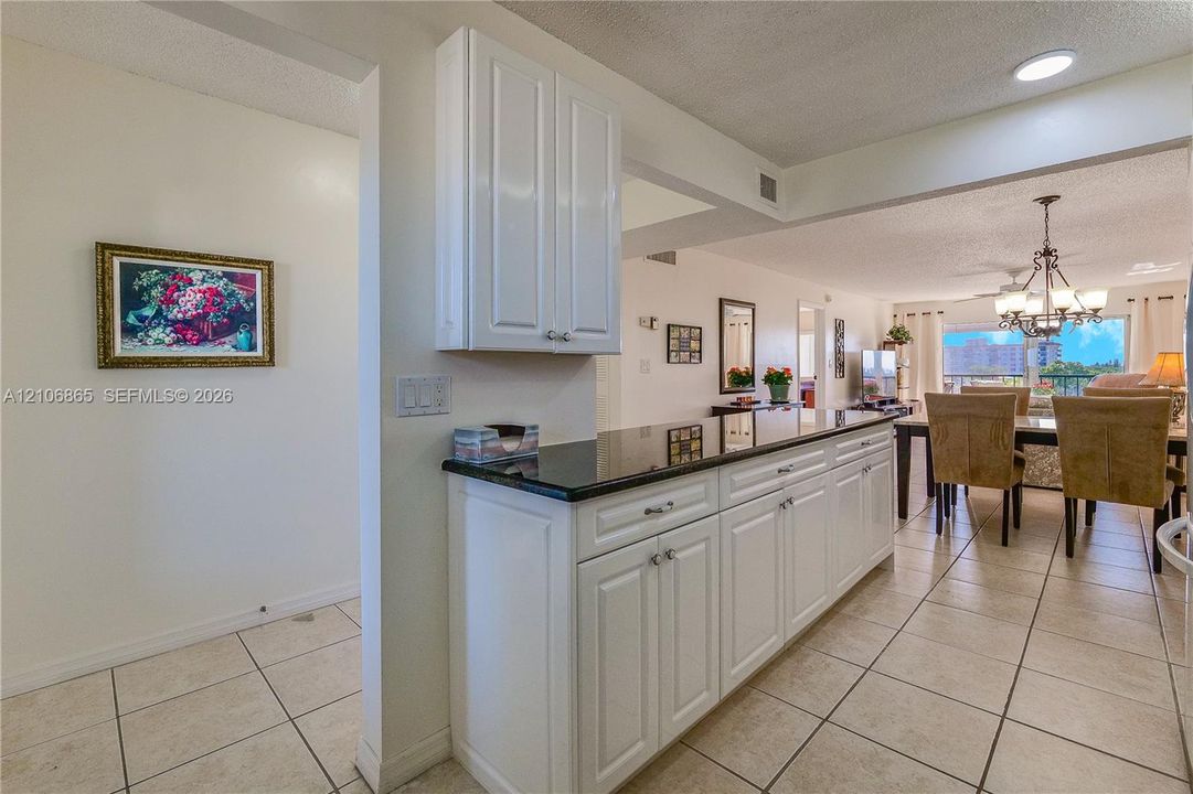 Kitchen area featuring white shaker-style cabinetry, black stone countertops, and tile flooring