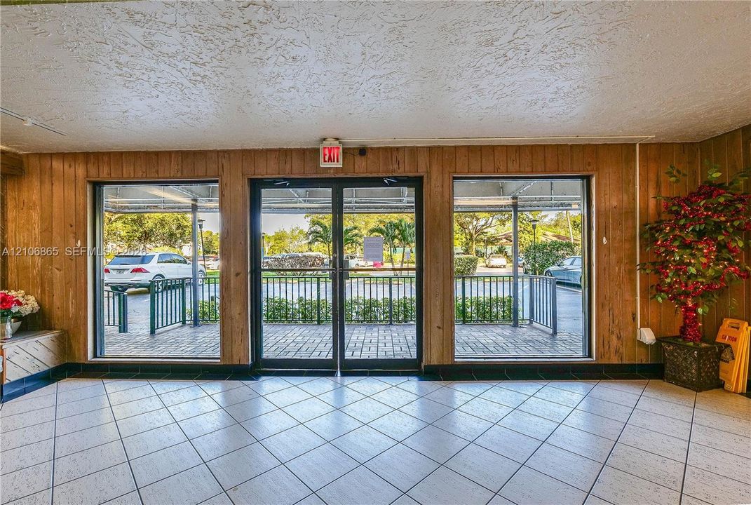 Double-door glass entrance with floor-to-ceiling side panels, wood-paneled walls, and tiled flooring