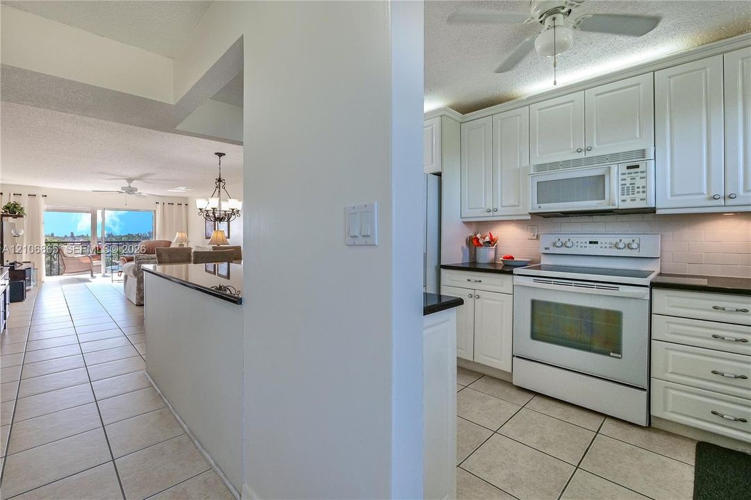 Kitchen featuring white shaker-style cabinetry, a dark stone countertop, an integrated microwave, a slide-in range, and ceramic tile flooring