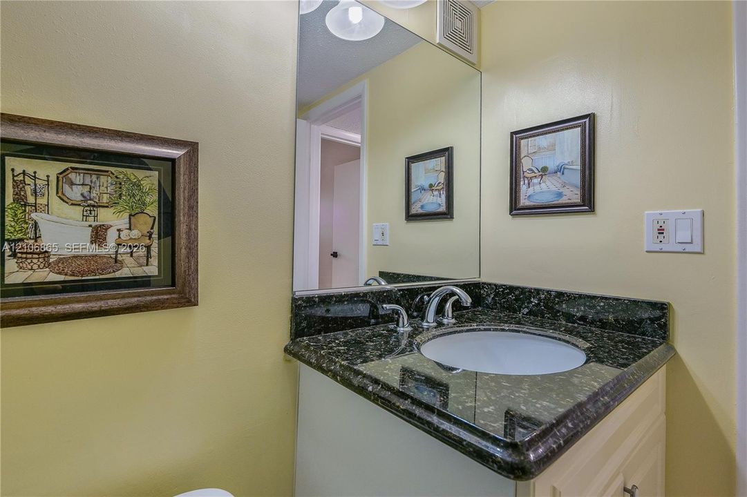 Vanity featuring a dark, polished stone countertop with an integrated white undermount sink and a polished chrome gooseneck faucet, complemented by a large wall-mounted mirror
