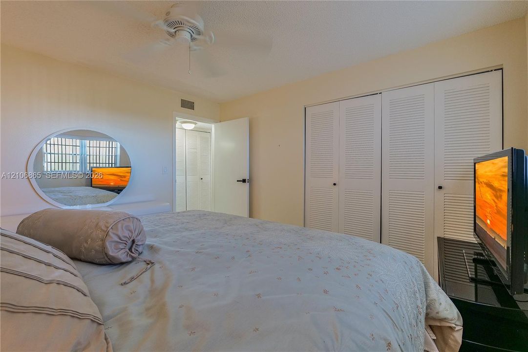 Room featuring dual-panel louvered closets, a circular wall-mounted mirror, and a ceiling fan with integrated lighting