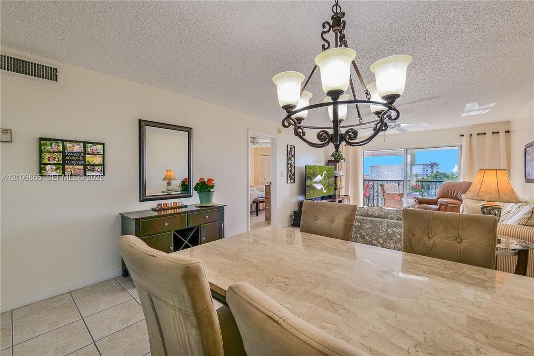 Ornamental multi-light chandelier, neutral ceramic tile flooring, and large sliding glass doors providing outdoor access