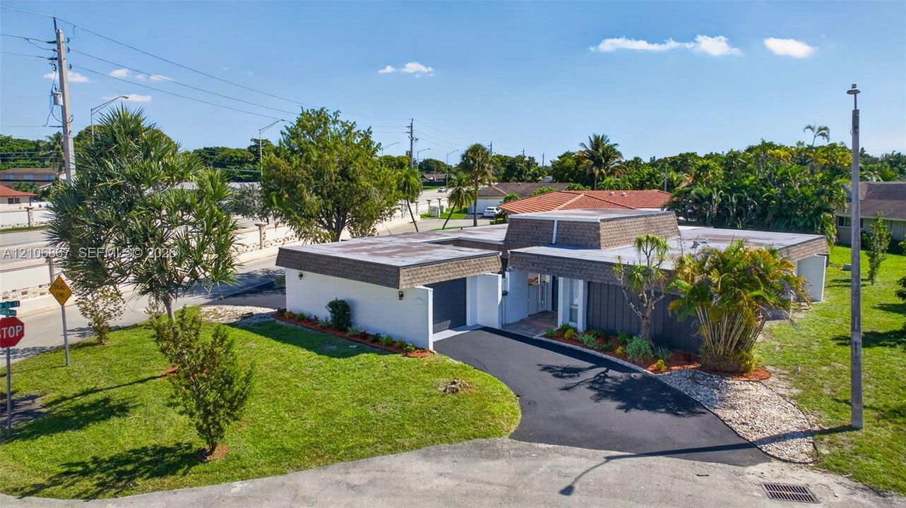 Mid-century modern exterior featuring a flat roofline with textured mansard detailing, white stucco façade, attached garage, and a paved driveway
