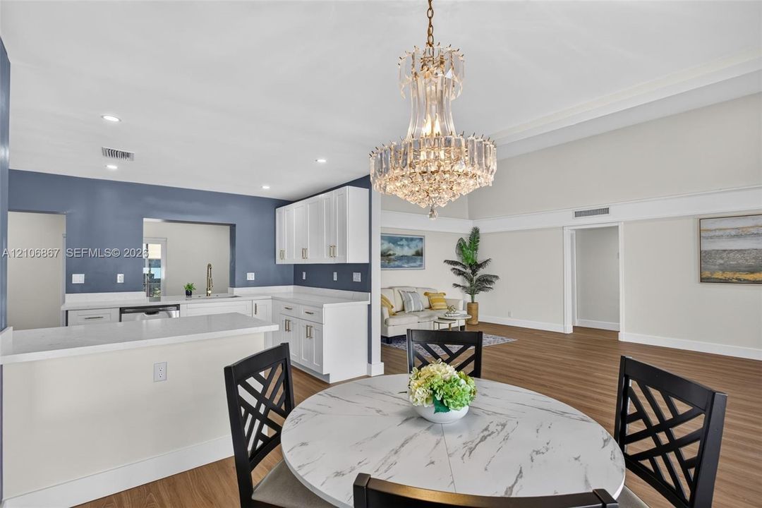 Vaulted ceilings, crystal chandelier, white cabinetry, quartz countertops, and wood-finish flooring