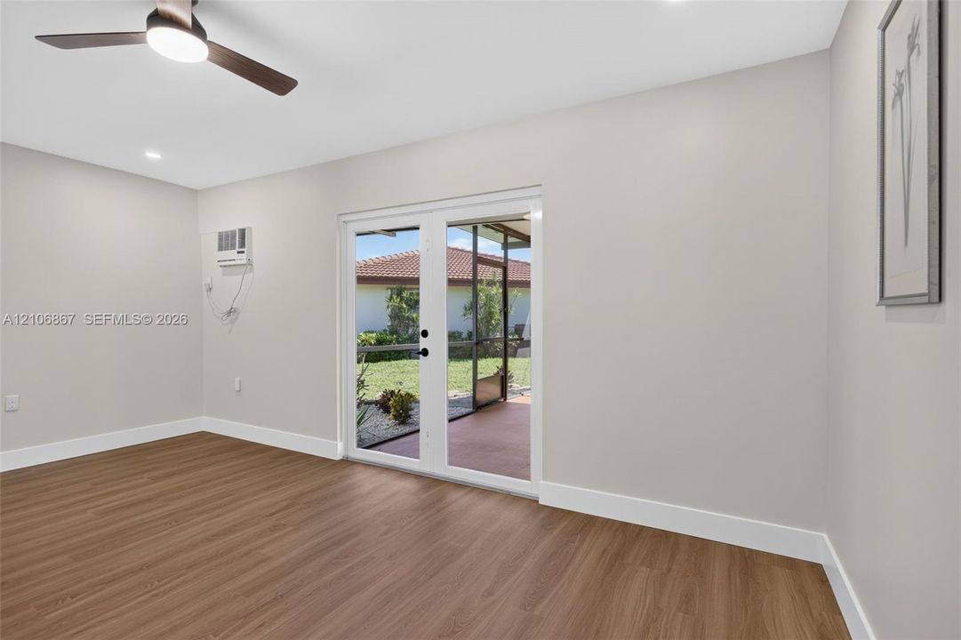 Neutral-toned interior featuring wood-finish flooring, a contemporary ceiling fan, and double glass-paned doors leading to a screened outdoor area