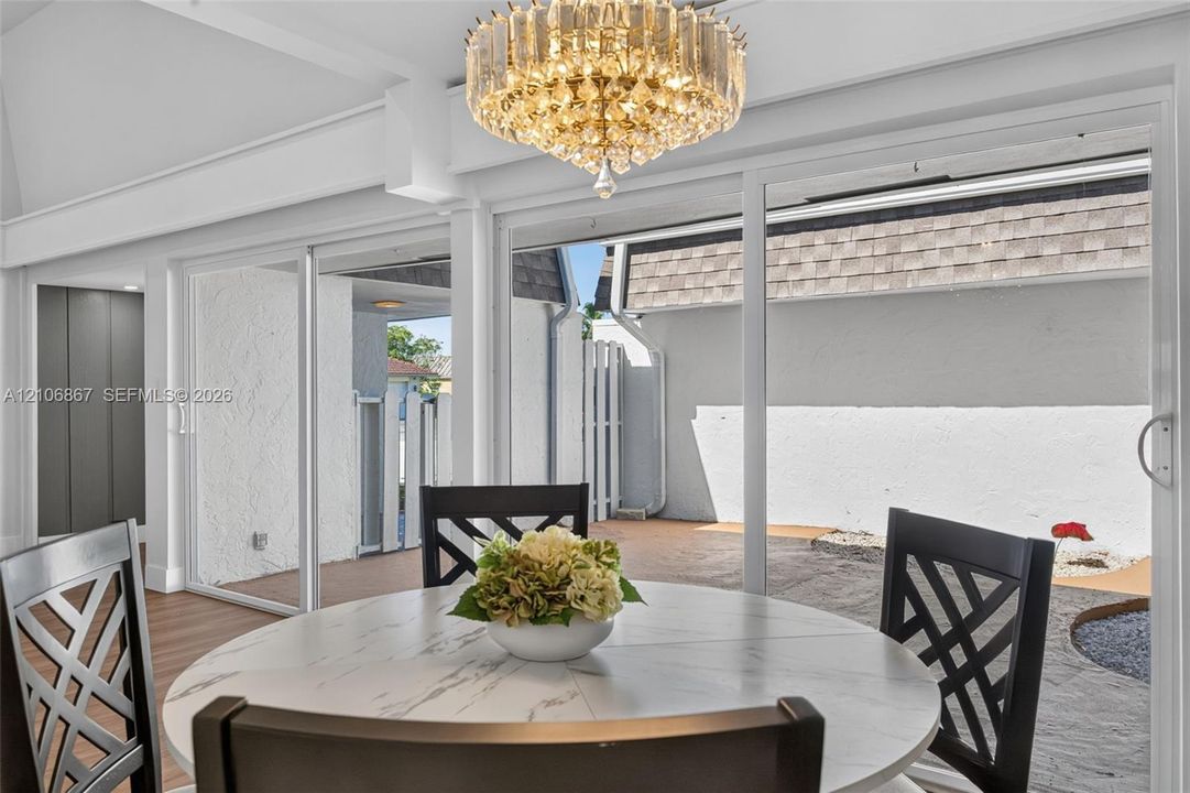 Vaulted ceiling featuring a statement crystal chandelier, wood-finish flooring, and expansive triple-panel sliding glass doors