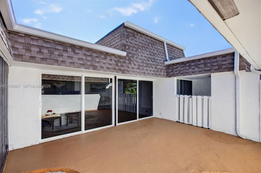 Covered patio featuring textured exterior walls, multiple sliding glass doors, shingle roof detailing, and a white privacy partition