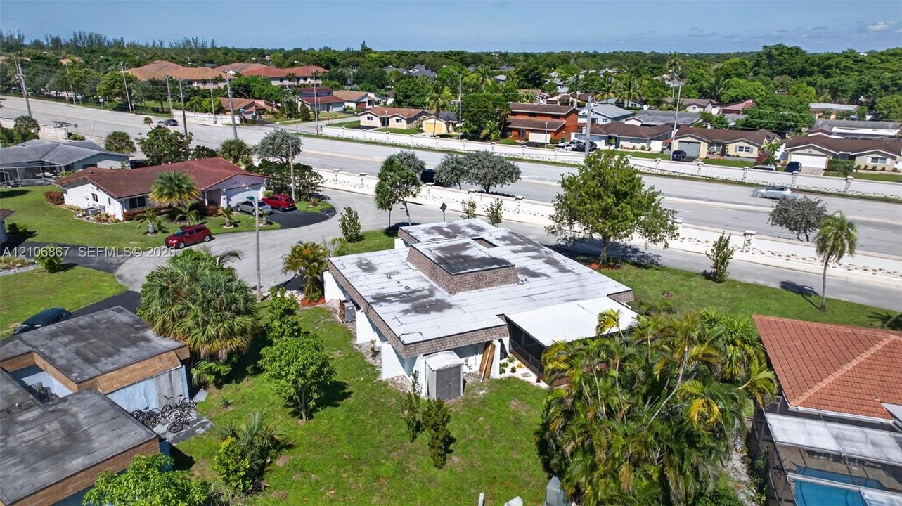 Aerial perspective of a detached property featuring a flat roofline, integrated screened-in patio, and extensive lawn area with mature palm trees
