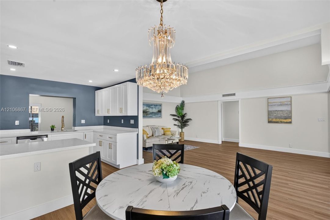 Kitchen featuring crisp white cabinetry, light-toned countertops, and a prominent crystal chandelier, complemented by wood-finish flooring and recessed lighting